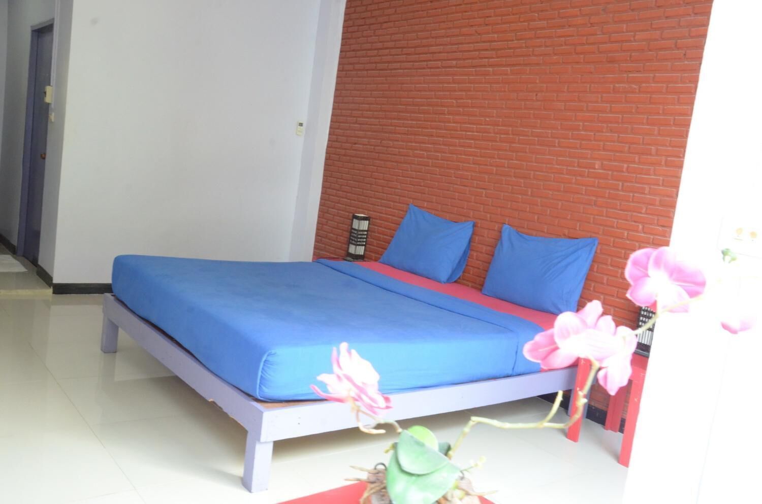 A bed with blue bedding and two pillows, a red brick wall, and a white door in the background.