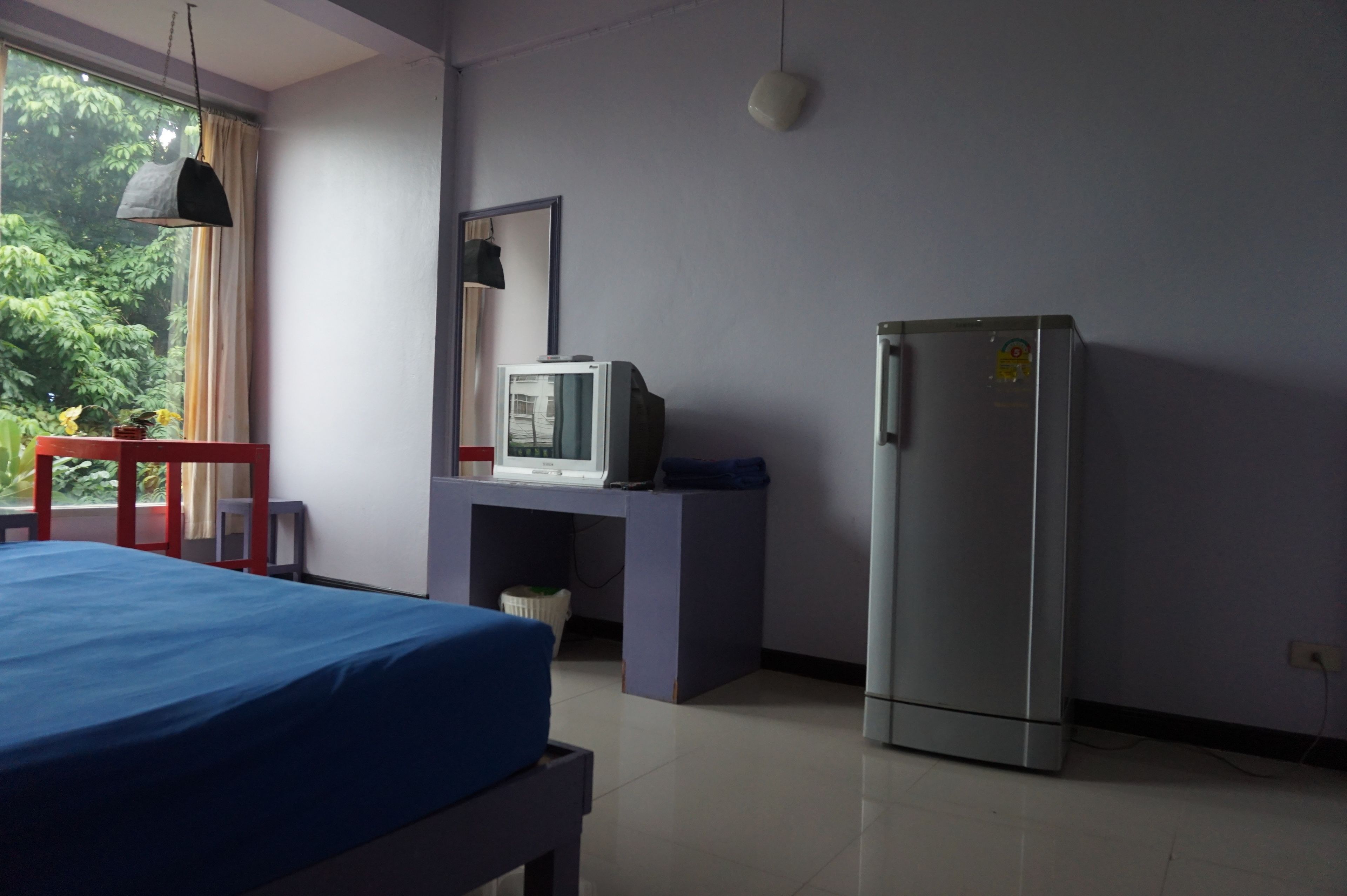 A room with a bed, a desk with a television, a refrigerator, and a window with curtains.