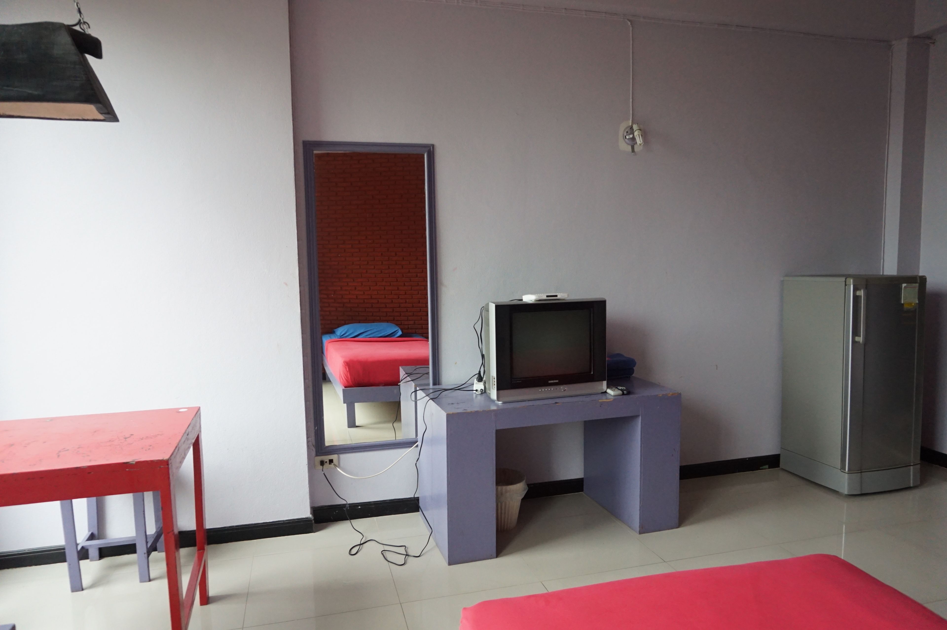 Een kamer met een bed, een televisie op een standaard, een koelkast en een tafel.