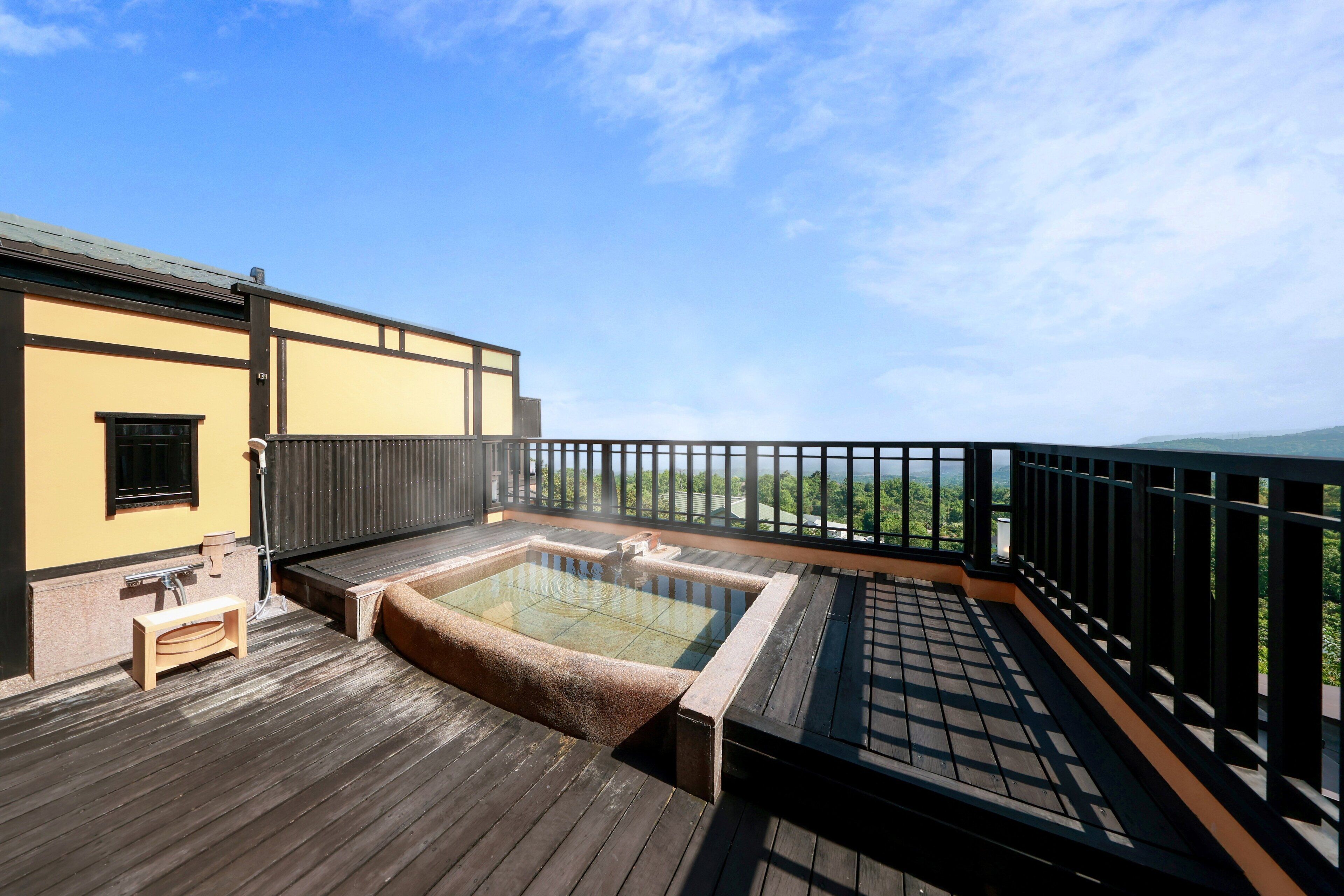 Una terraza de madera con un jacuzzi y un pequeño banco, con vistas a un paisaje verde.