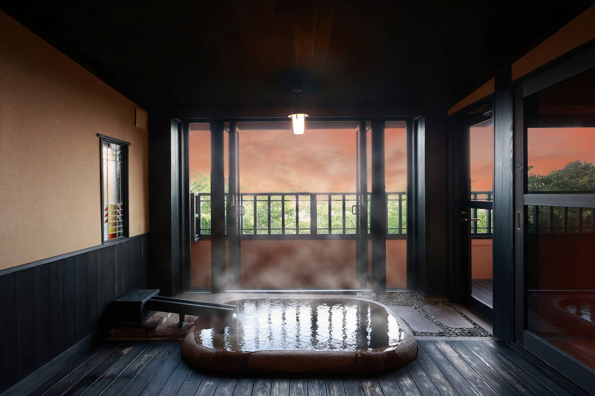 A hot spring bath with a wooden deck, large windows, and a view of greenery.