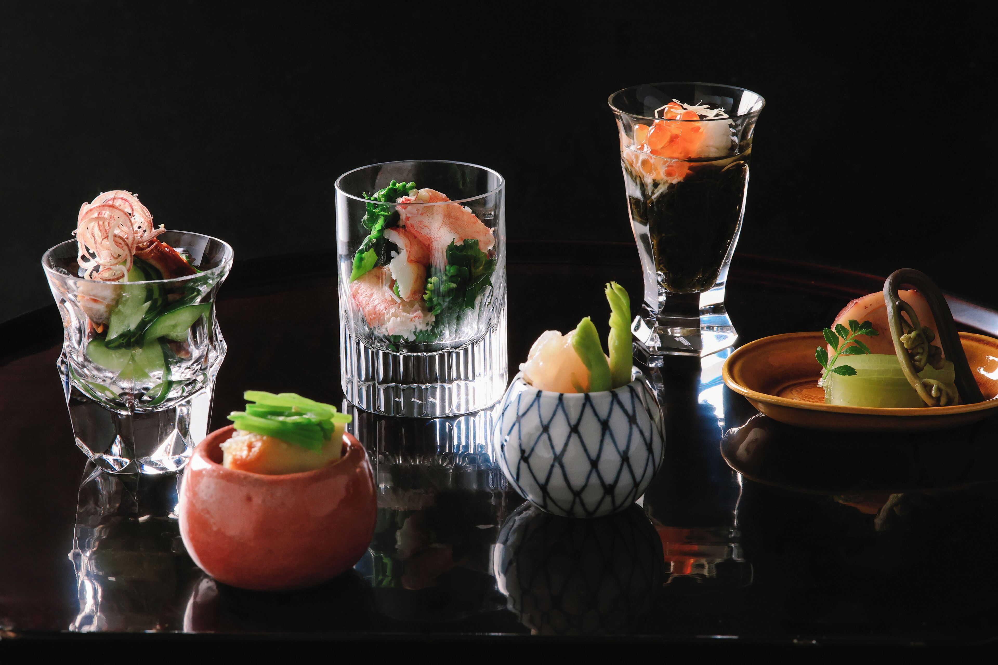 A variety of glassware containing seafood dishes, arranged on a reflective surface.