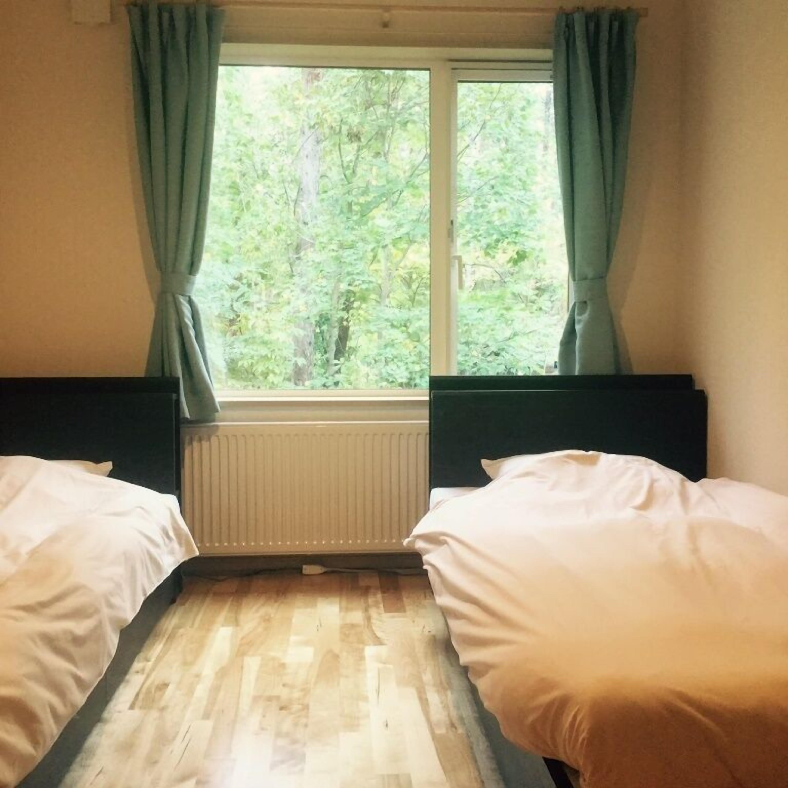 Una habitación con dos camas, un ventanal con cortinas y un radiador.