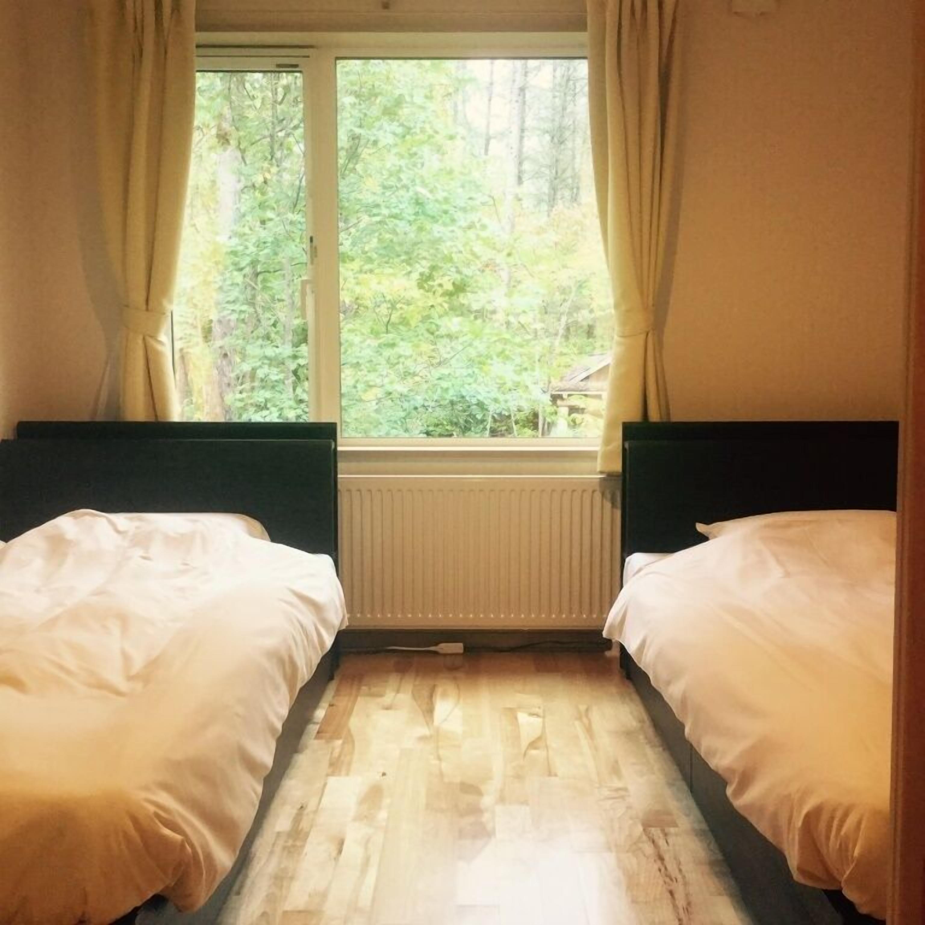 Habitación con dos camas, una ventana con cortinas, un radiador y vistas a árboles.