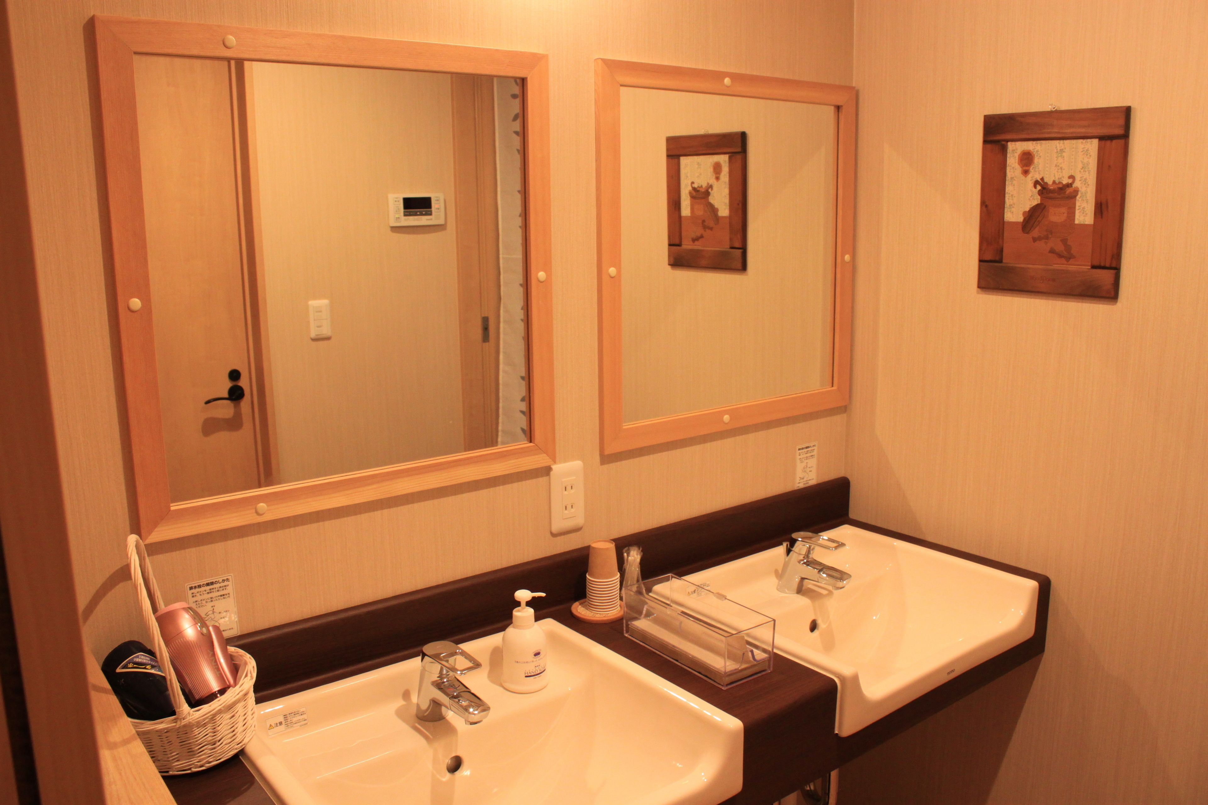 Un baño de hotel con dos lavamanos, espejos y una cesta con artículos de aseo.
