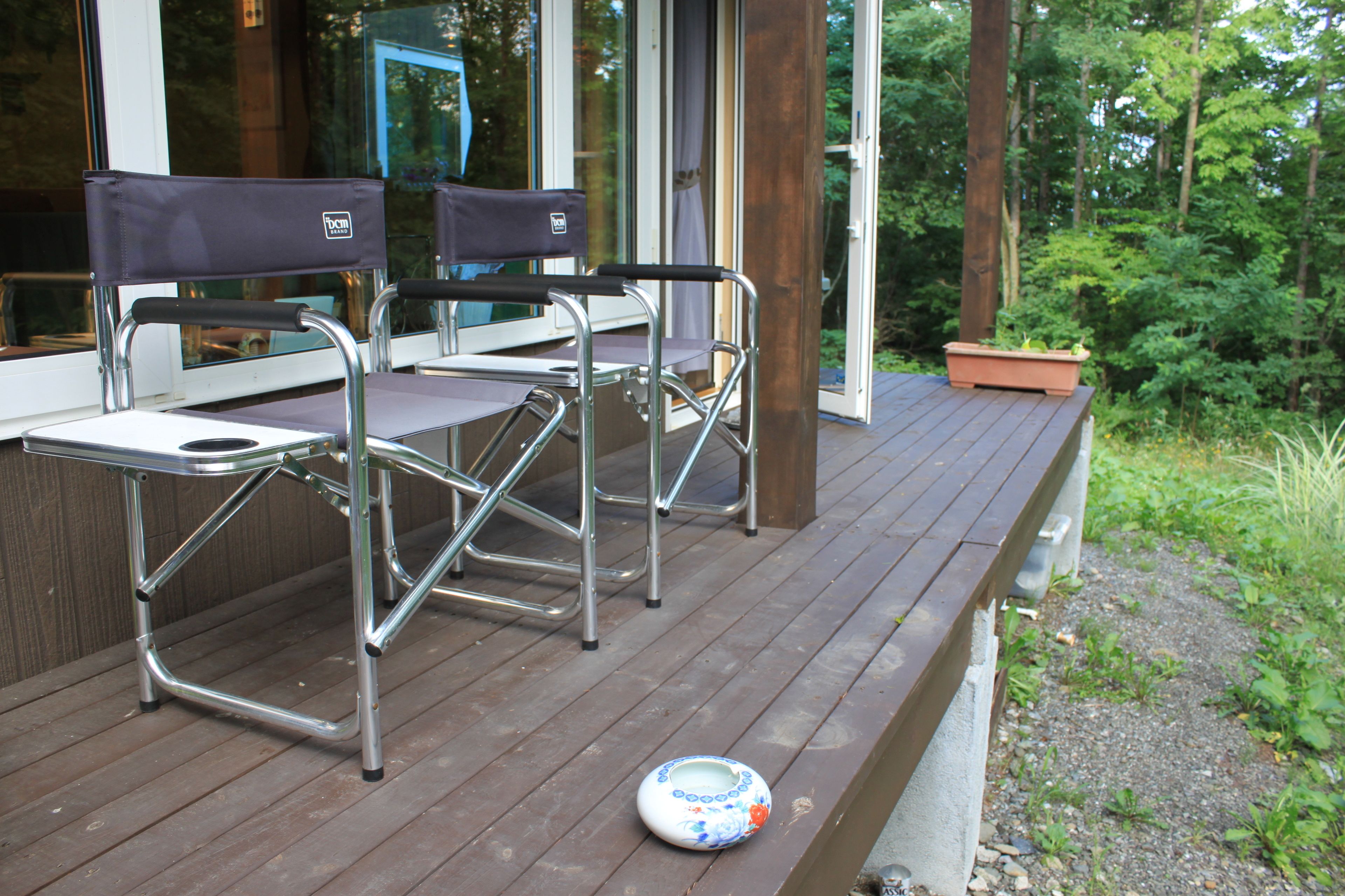 A deck with two chairs and a table, surrounded by a wooden deck and greenery.