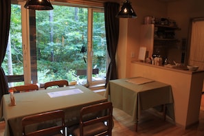 Un comedor con una mesa y sillas, una pequeña cocina y vistas a un bosque a través de un ventanal grande.