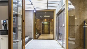 A modern elevator interior with glass doors, a control panel, and a carpeted floor. - Hotel Arozo (Seoul)