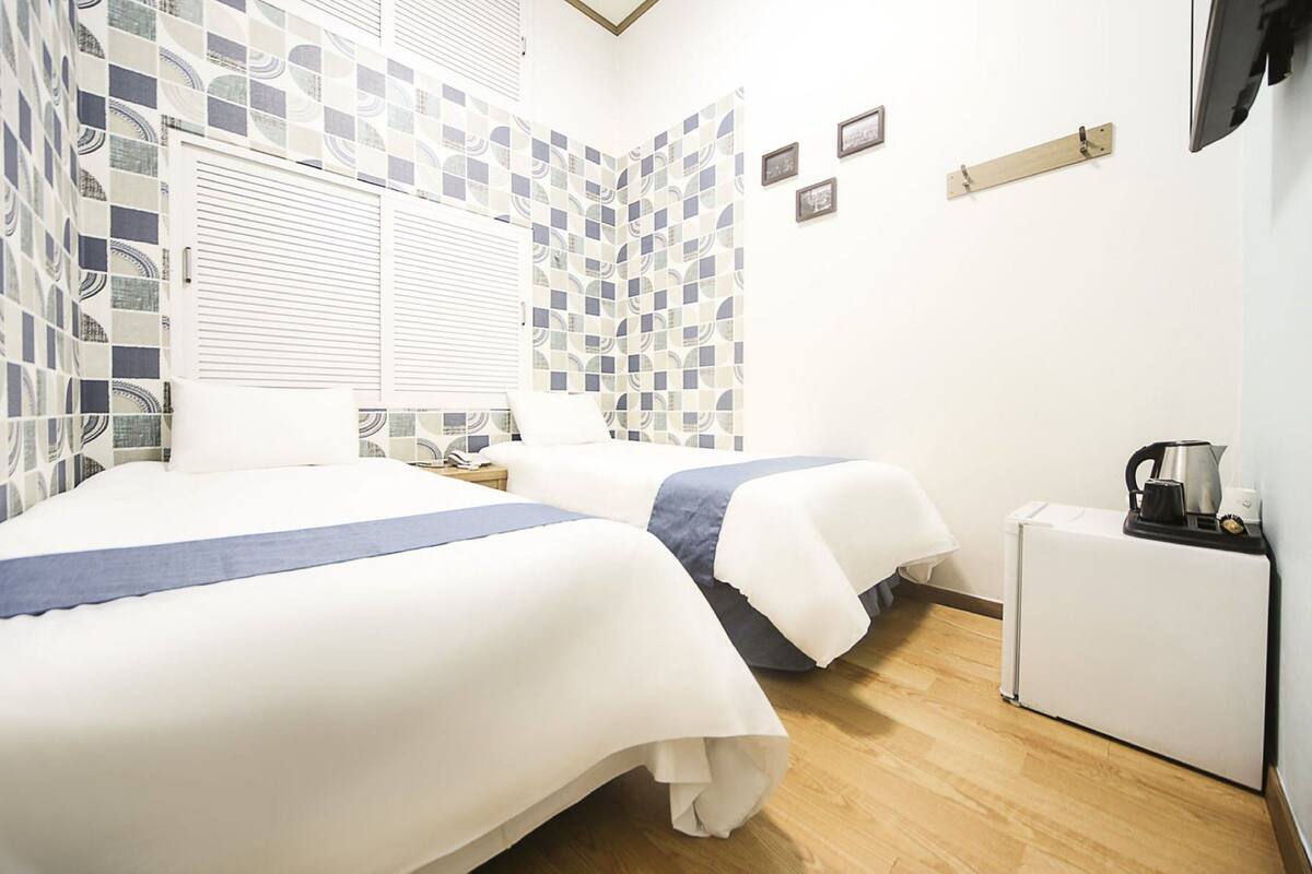 A hotel room with two beds, a small desk, and a refrigerator.