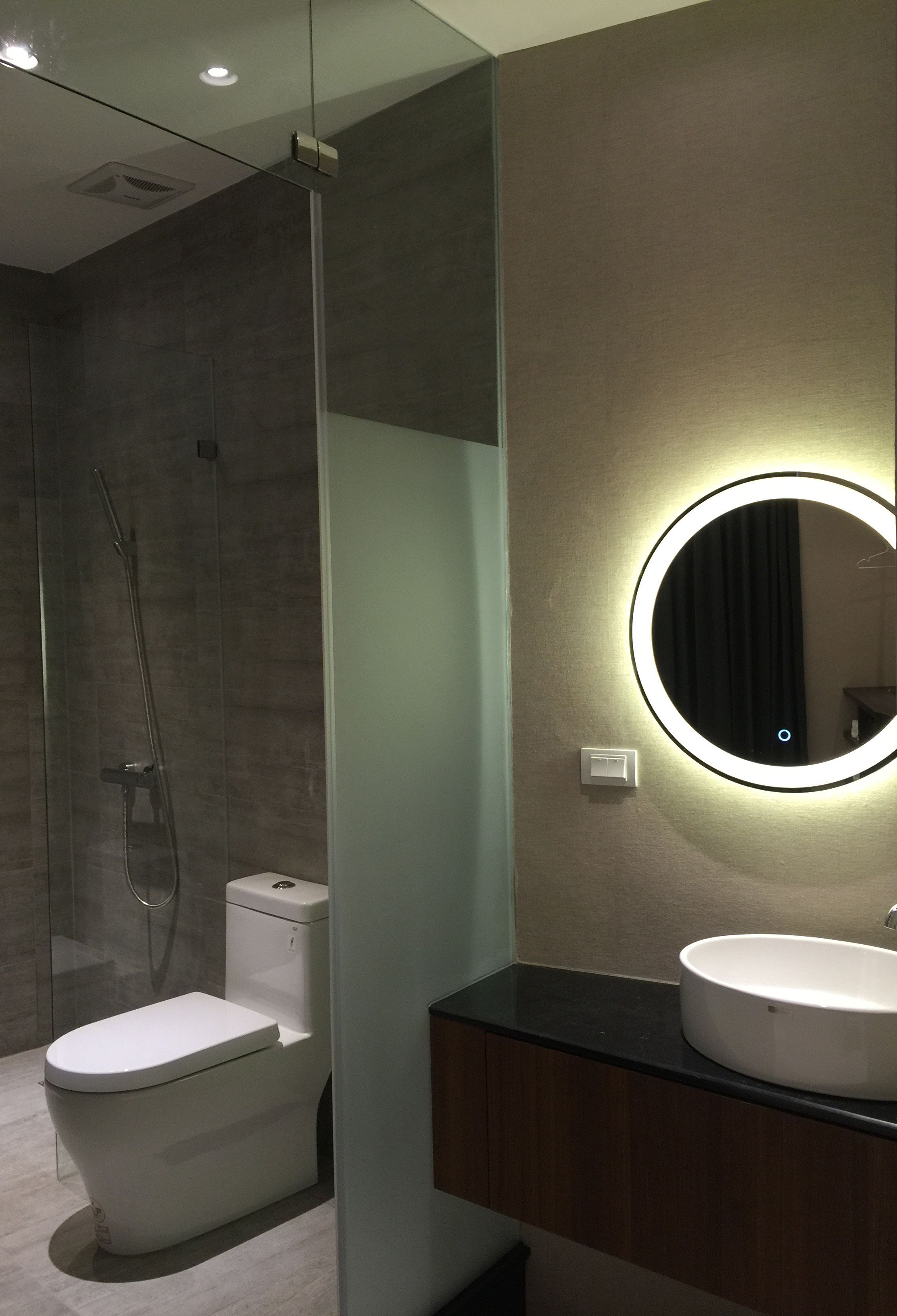 A modern bathroom with a glass-enclosed shower, a toilet, and a vanity with a round mirror.