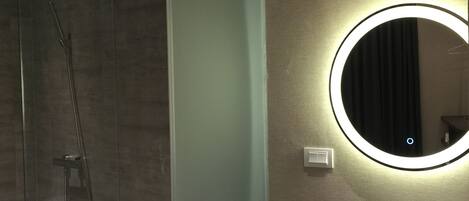A modern bathroom with a glass-enclosed shower, a toilet, and a vanity with a round mirror.