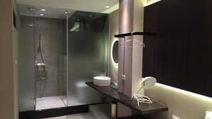 A modern bathroom with a glass shower enclosure, a round sink with a mirror, and a dark vanity with a towel rack. - Feliz Hotel Kenting (Hengchun)