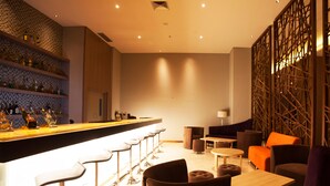 A modern bar area with a long counter, multiple stools, and a seating area with tables and chairs.