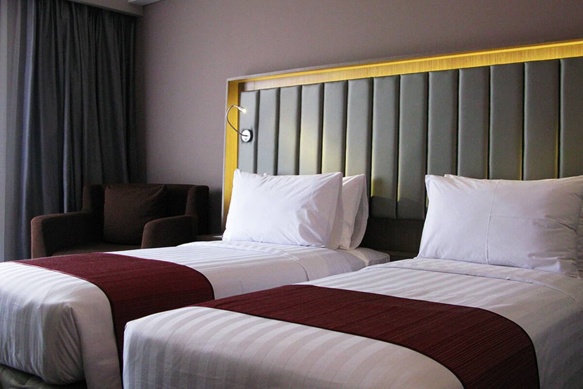 Una habitación de hotel con dos camas, una silla y un cabecero con paneles verticales.