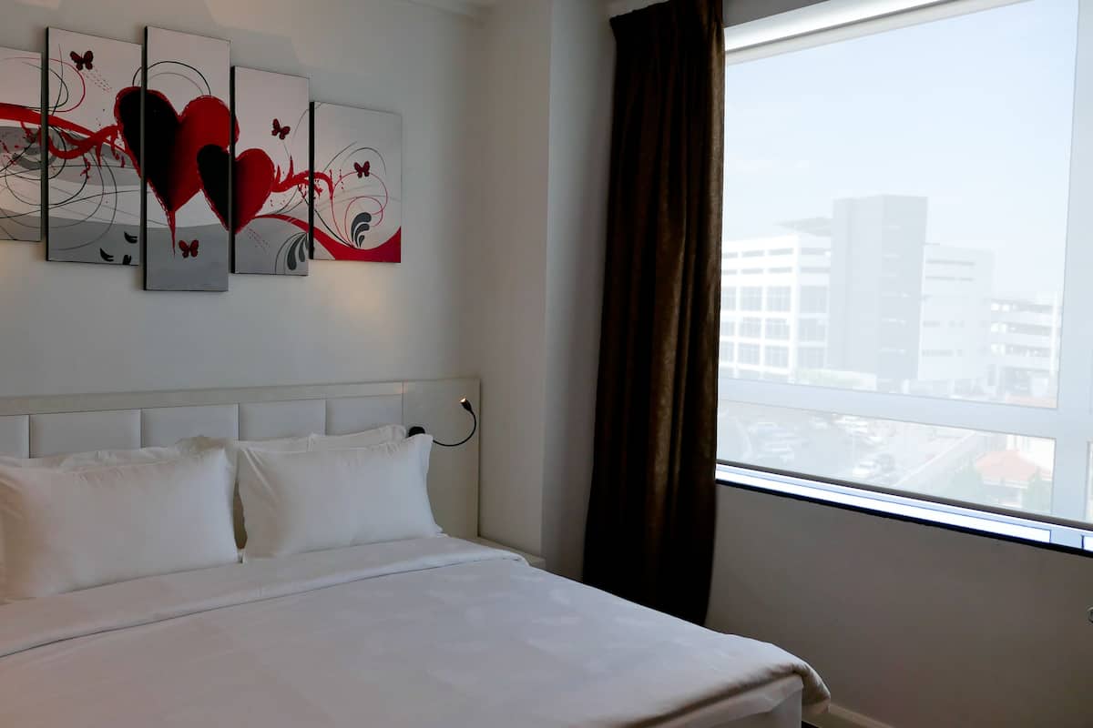 Ein Hotelzimmer mit Bett, weißer Bettwäsche, einem Kopfteil, einem Nachttisch mit Telefon und einem Fenster mit Vorhängen.