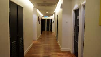 A hallway with wooden flooring, white walls, and black doors. There is a sign indicating the location of the elevator.
