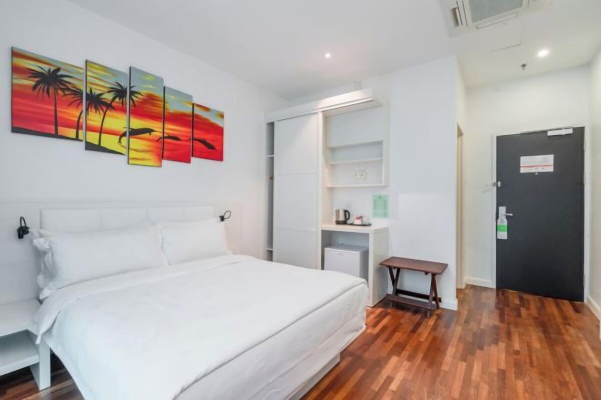 Una habitación de hotel con cama, un banco, un estante en la pared y una puerta.