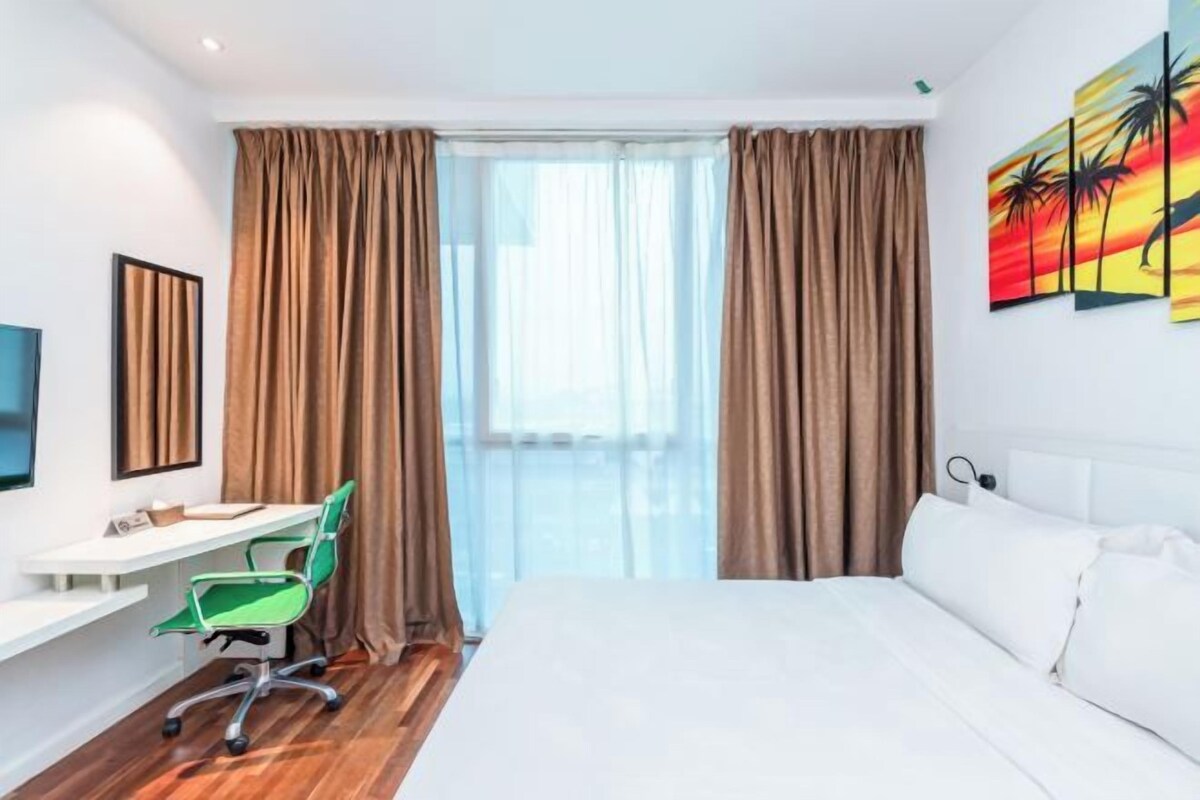 Una habitación de hotel con cama, escritorio con silla, televisor y ventana con cortinas.