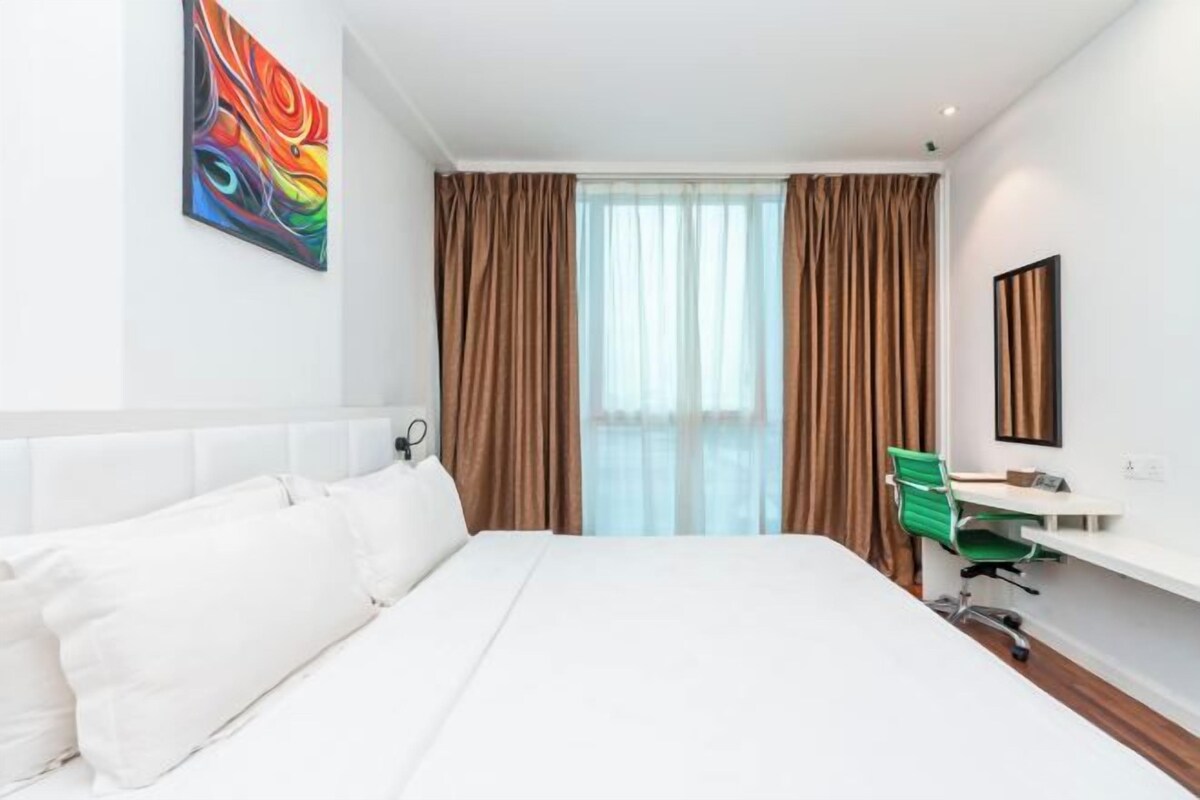 Habitación de hotel con una cama grande, un escritorio con silla, una ventana con cortinas y un cuadro en la pared.