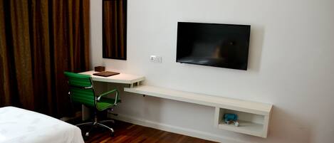 A hotel room with two beds, a desk with a chair, a TV mounted on the wall, and a shelf below the TV.