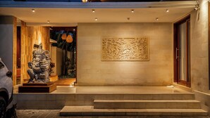Une entrée moderne ornée d’une statue en pierre, d’une grande œuvre d’art en relief et d’un véhicule garé à l’extérieur.