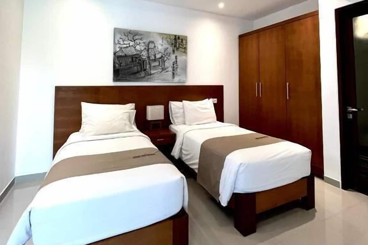 A modern hotel room with two beds, a wooden headboard, a nightstand, and a wardrobe.