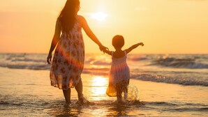 Une scène de coucher de soleil où l’on voit une personne et un enfant se tenant la main sur la plage.