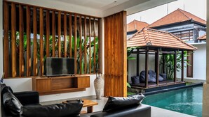 Un salon moderne doté d’un téléviseur, d’un canapé en cuir, d’un mur revêtu de panneaux en bois et offrant une vue sur une piscine et un espace de détente extérieur.