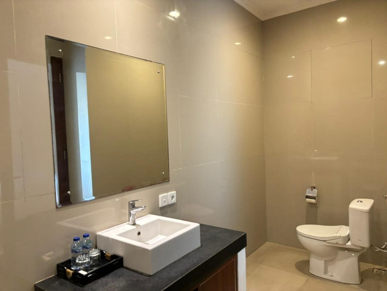 A modern bathroom with a large mirror, a white sink, and a toilet.