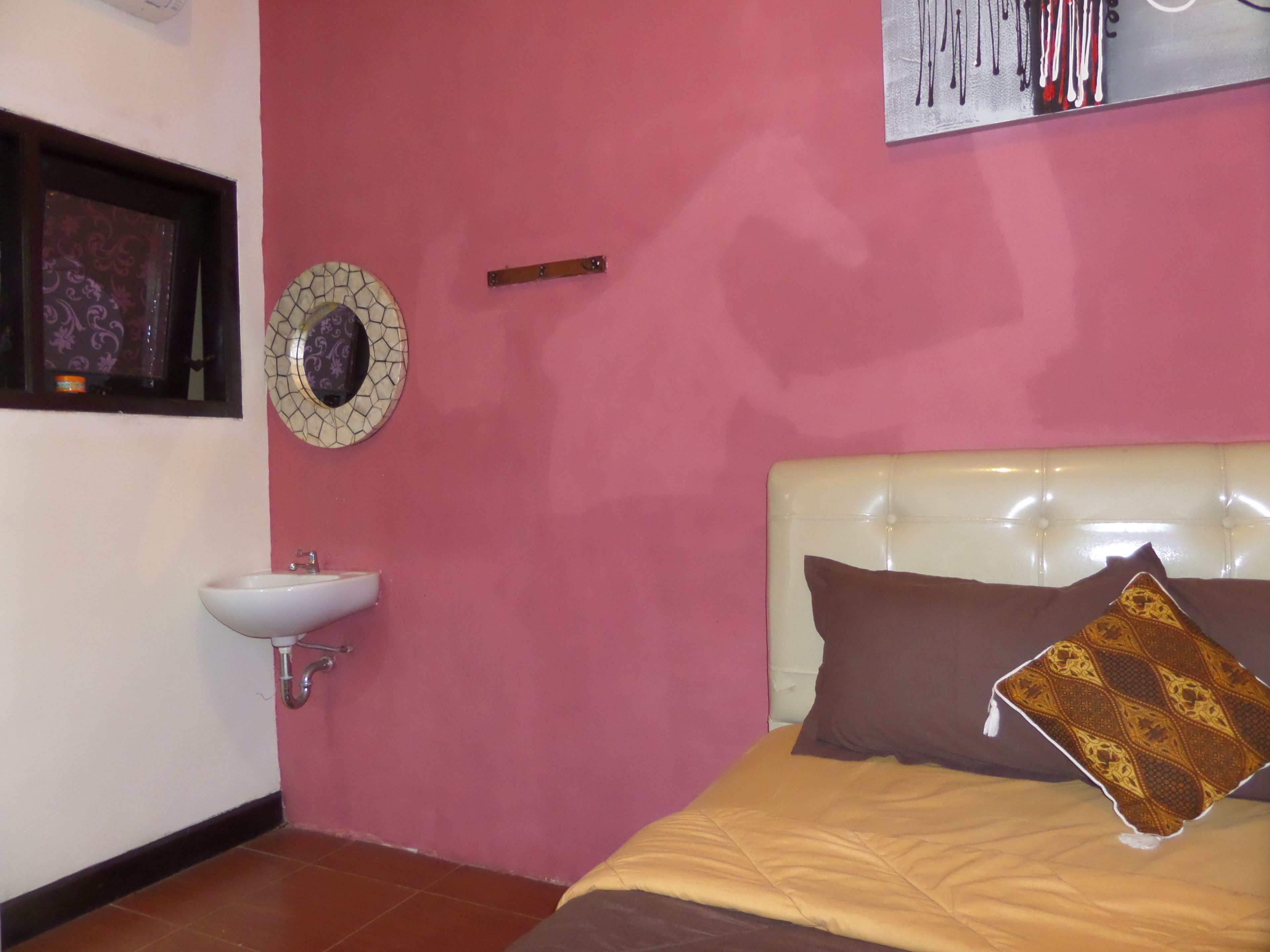 A bedroom with a bed, a bedside table, a wall-mounted mirror, and a wall-mounted sink.