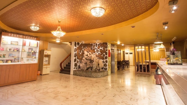 Un vestíbulo de hotel con piso de mármol, un mostrador de recepción, una escalera y un techo con diseño.