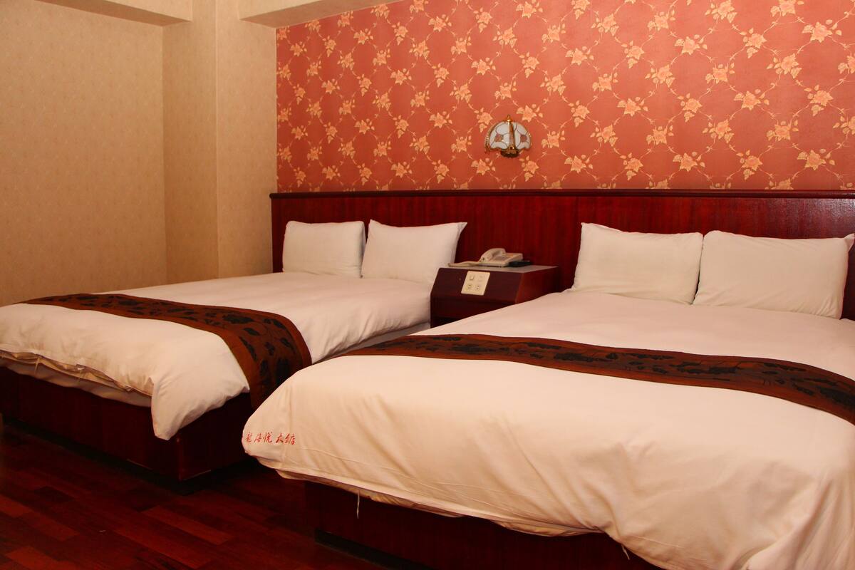 Two single beds with wooden headboards, a nightstand with a telephone, and a floral-patterned wall.