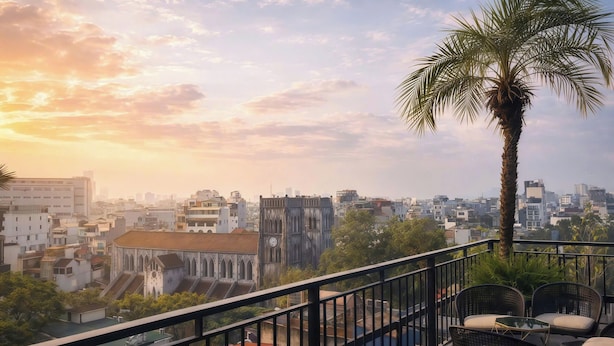 Un balcon avec des chaises et un palmier, donnant sur un paysage urbain avec des immeubles et une église.