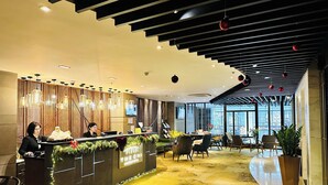 Un espace d’accueil d’hôtel au design moderne, comprenant un comptoir d’accueil, un coin salon et de grandes fenêtres.