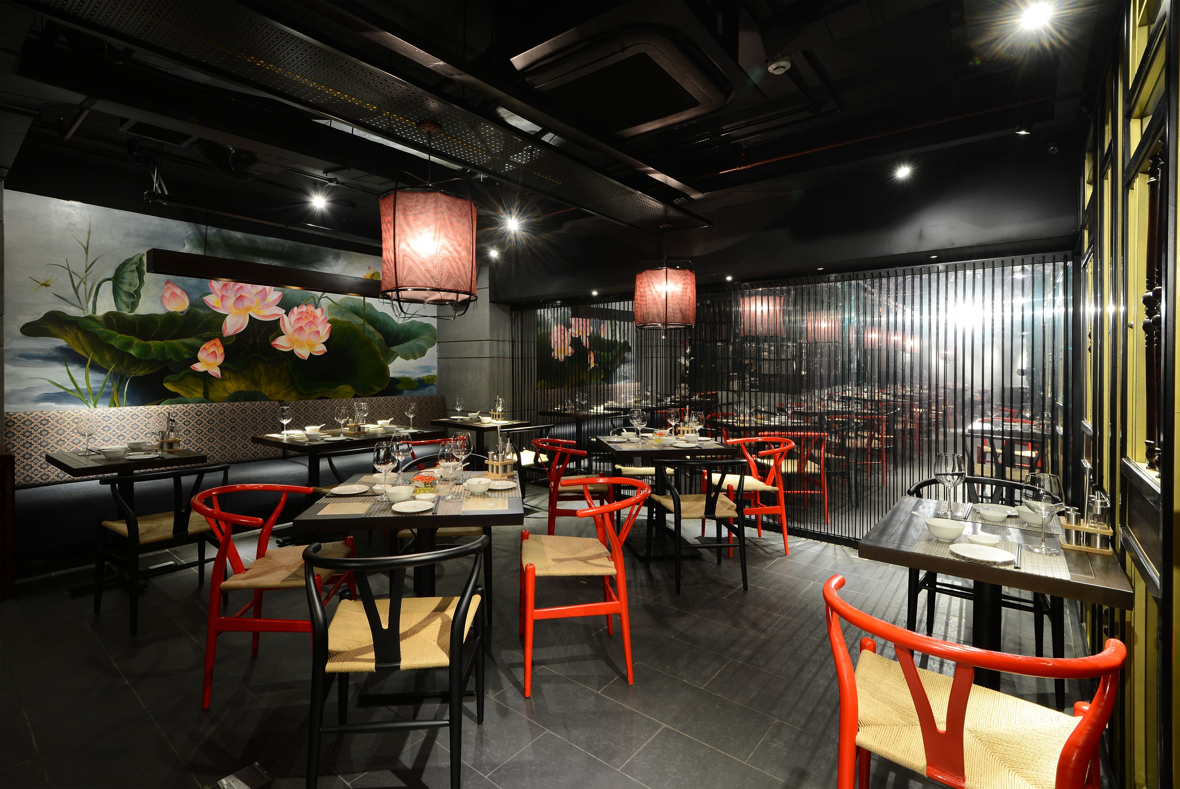 L’intérieur d’un restaurant, avec ses tables et ses chaises, une fresque représentant des fleurs de lotus et des lanternes suspendues.