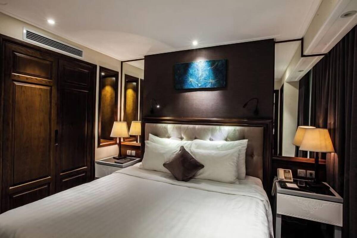 Une chambre d’hôtel avec un grand lit, une armoire en bois, des lampes de chevet et une œuvre d’art accrochée au mur.