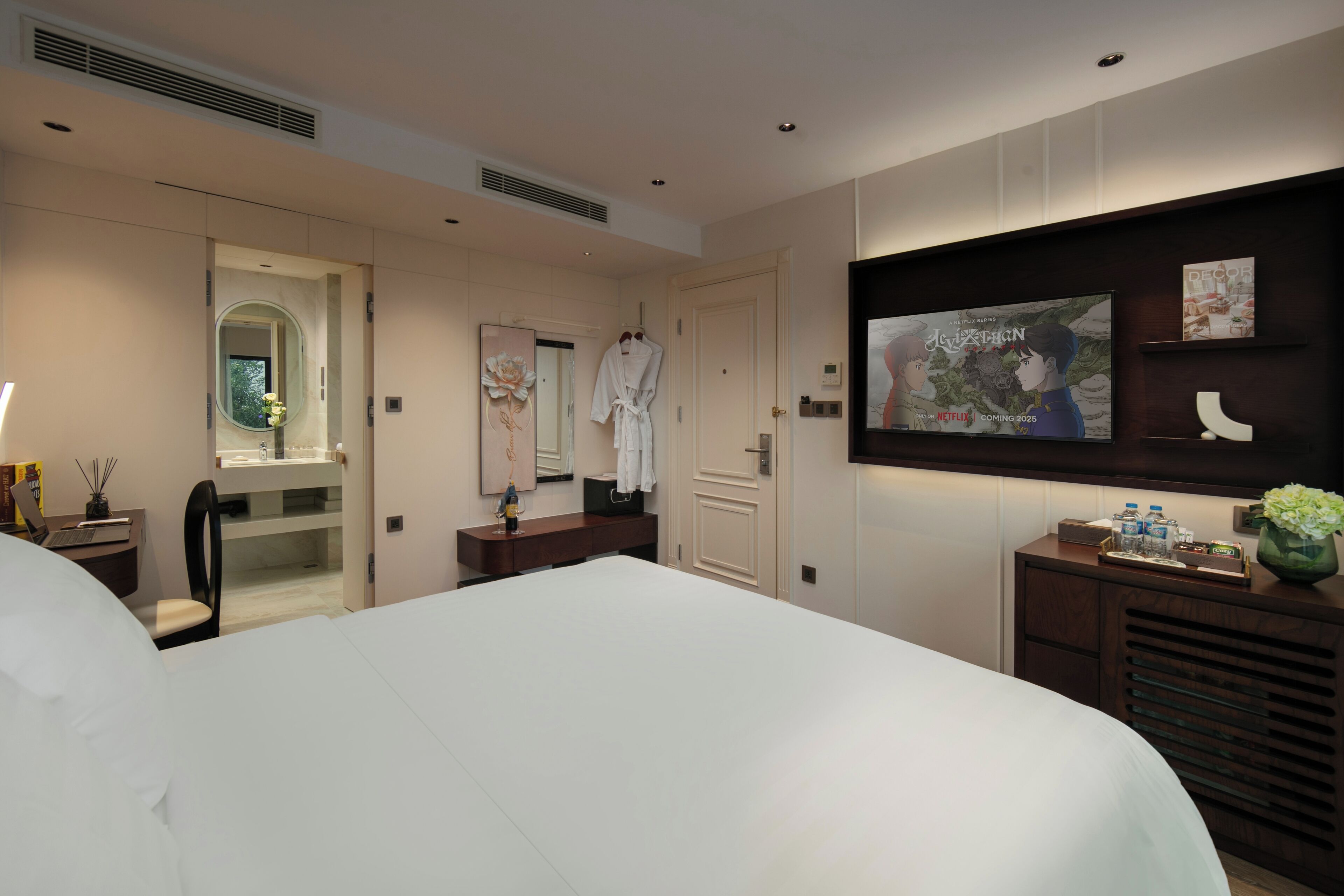 Una camera d'albergo moderna con un letto grande, una TV a parete, una toeletta con specchio e una piccola scrivania con sedia.