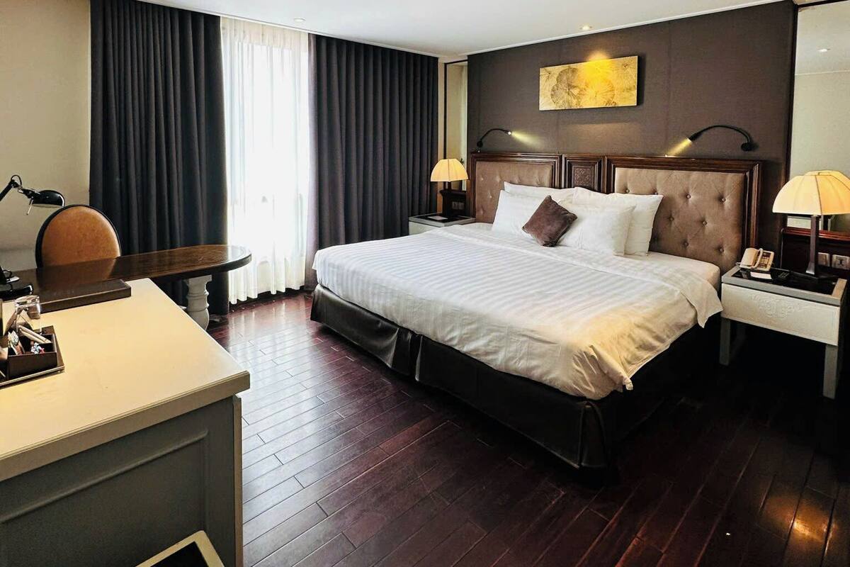 Une chambre d’hôtel avec un grand lit, un bureau, une chaise, une table de chevet et un tableau au mur.