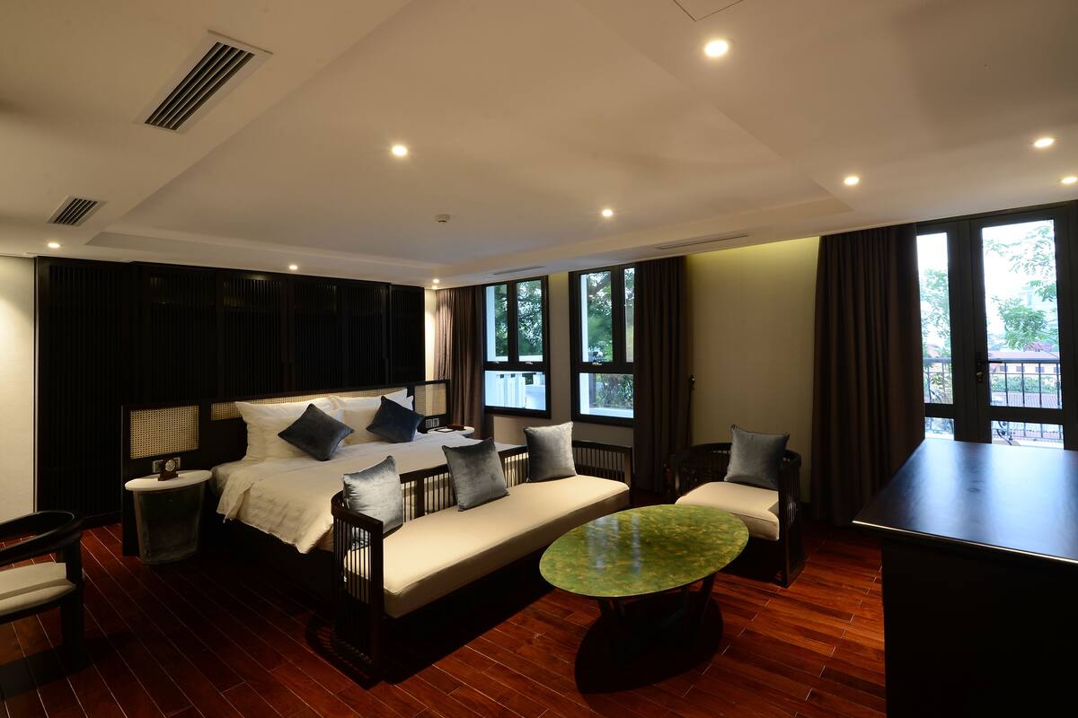 Une chambre d’hôtel moderne, dotée d’un grand lit, d’un canapé, d’une petite table et offrant une vue sur l’extérieur grâce à de grandes fenêtres.