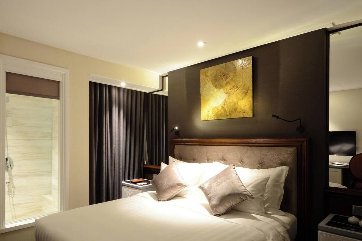 Une chambre d’hôtel avec un lit, une table de chevet, un miroir et une fenêtre avec des rideaux.