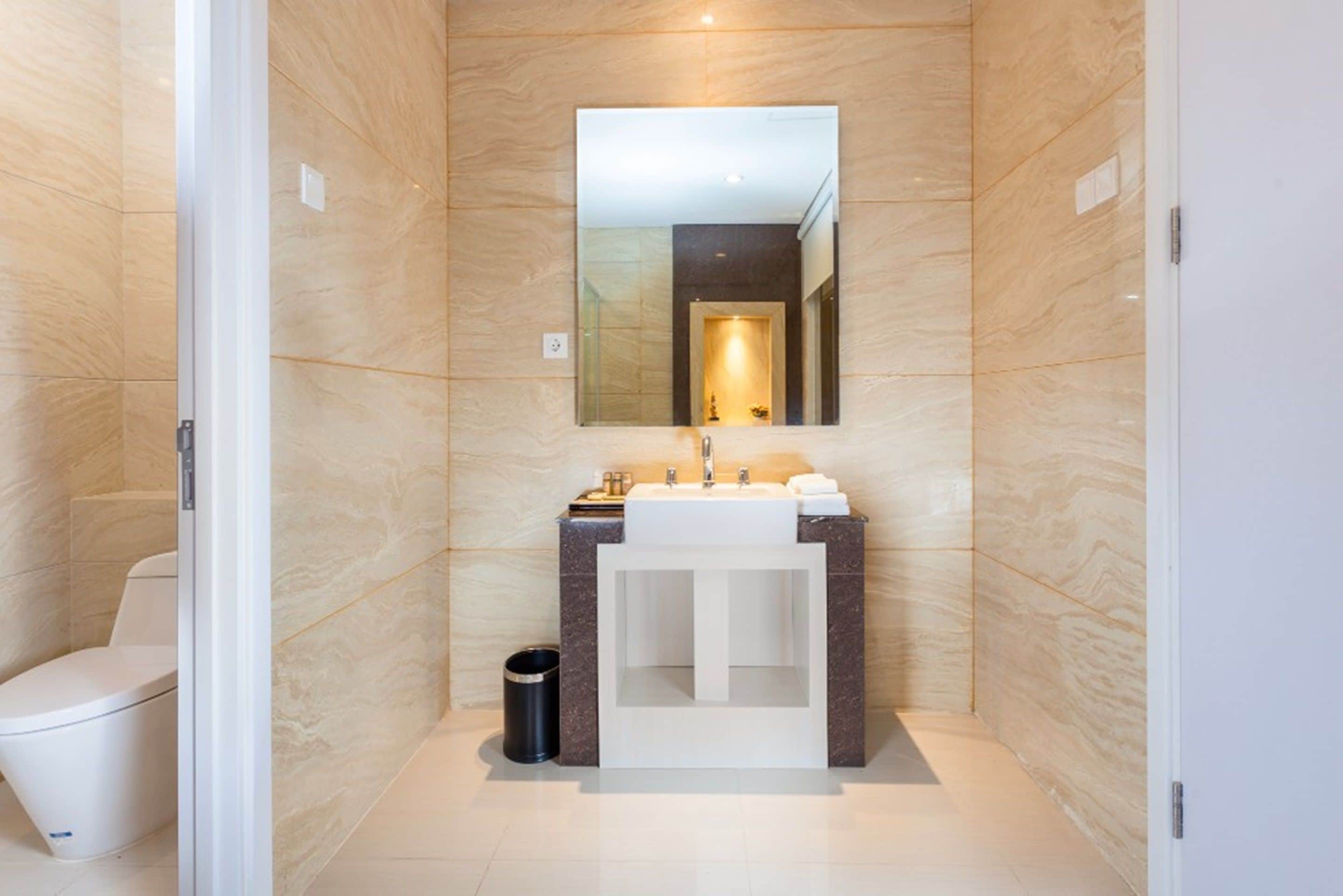 A modern bathroom with a marble wall, a white sink, a mirror, and a toilet.