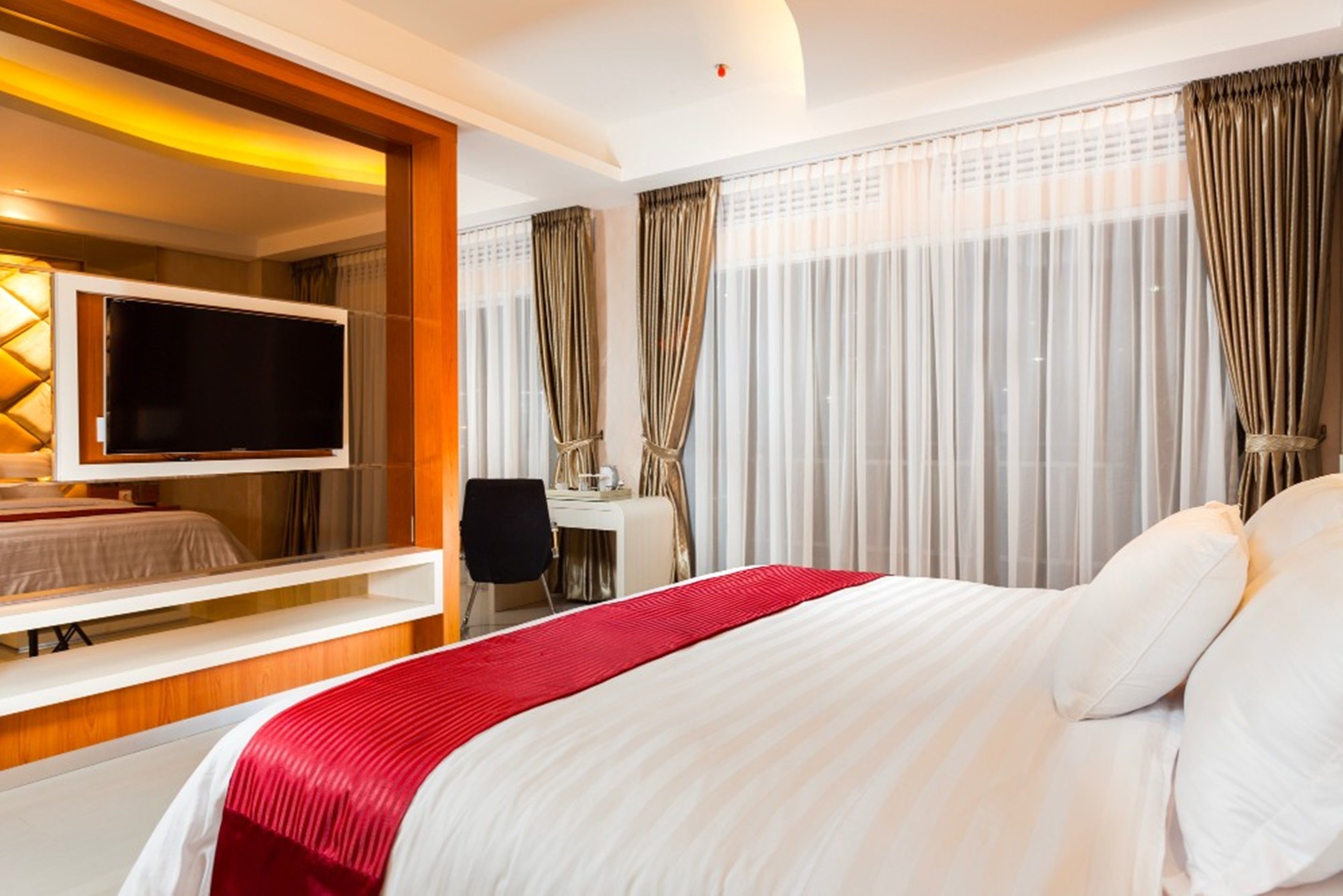 A hotel room with a bed, a desk, a chair, a television, and curtains.
