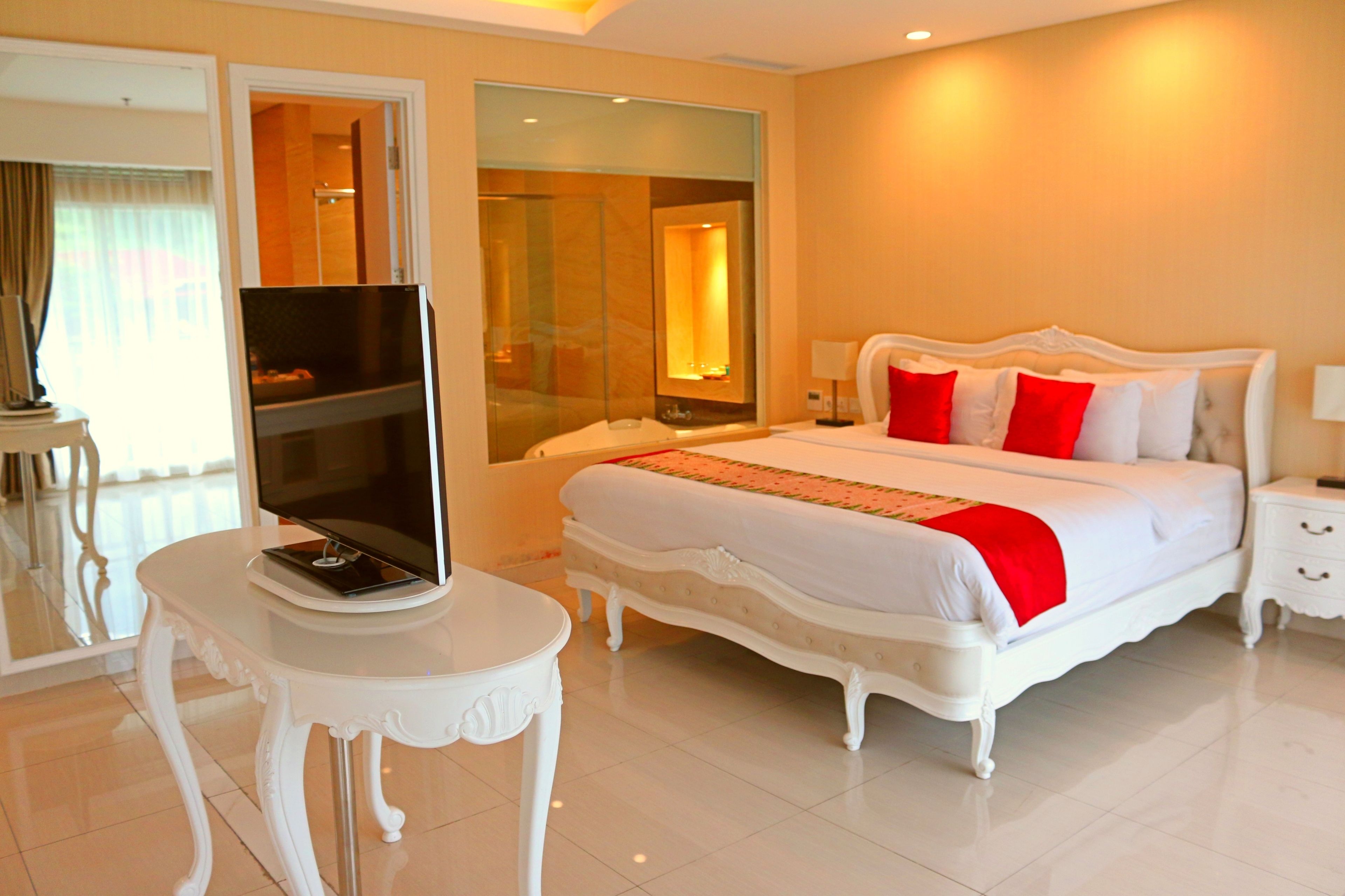 A hotel room with a large bed, a television on a white table, and a glass-enclosed shower area.