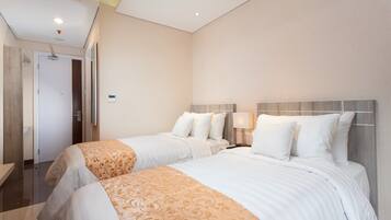 A hotel room with two beds, a wooden headboard, a bedside table with a lamp, and a door leading to a bathroom.