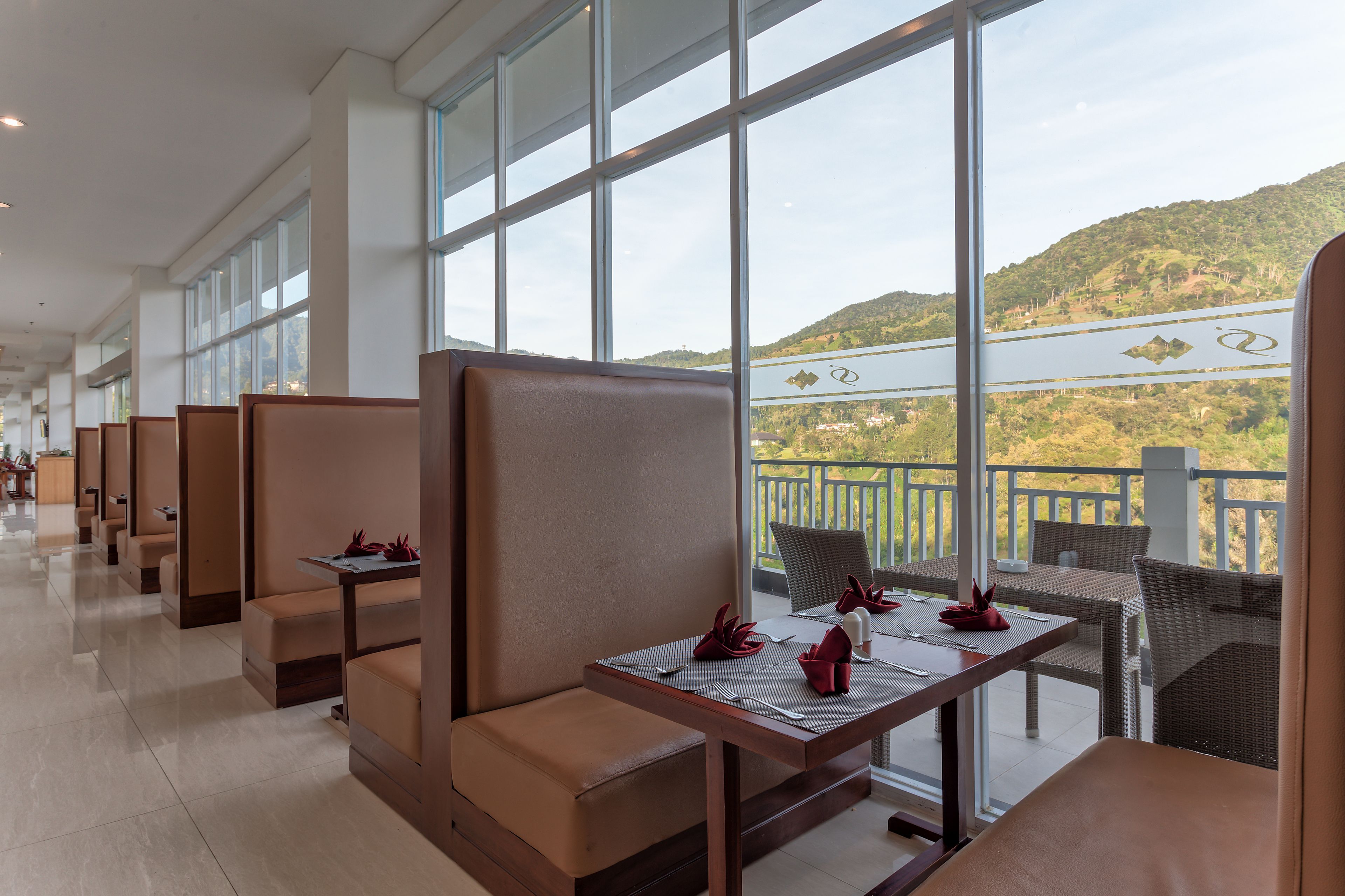 A hotel lobby with seating areas, large windows, and a view of a hilly landscape.