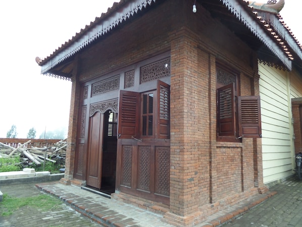 A traditional brick building with wooden doors and shutters, featuring intricate carvings and a tiled roof.