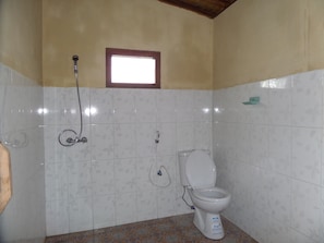 A bathroom with a toilet, shower, and a small window. - Villa Adas (Ngadisari)