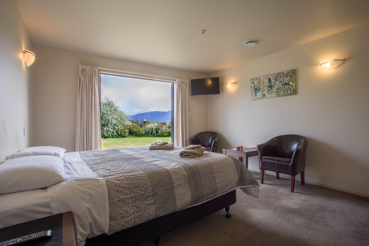 Une chambre avec un grand lit, une chaise, une petite table et un téléviseur fixé au mur.