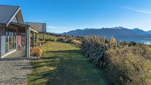 Une maison moderne dotée d’un porche abrité, d’une allée en gravier et offrant une vue sur les montagnes et un lac.