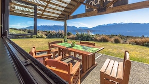 Un espace extérieur aménagé, abrité et doté de tables et de chaises, offrant une vue panoramique sur un paysage magnifique, avec des montagnes et un lac.